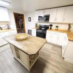 Bright rustic kitchen with white cabinets, wood countertops, and central island in a Fairbanks adventure lodge