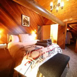 Rustic cabin bedroom with tribal blanket, soft lighting, and wooden walls in a Fairbanks, Alaska treehouse rental.