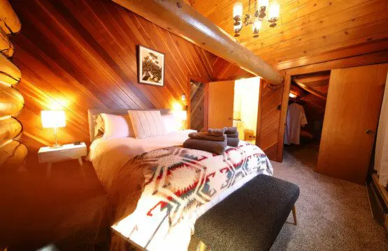 Rustic cabin bedroom with tribal blanket, soft lighting, and wooden walls in a Fairbanks, Alaska treehouse rental.