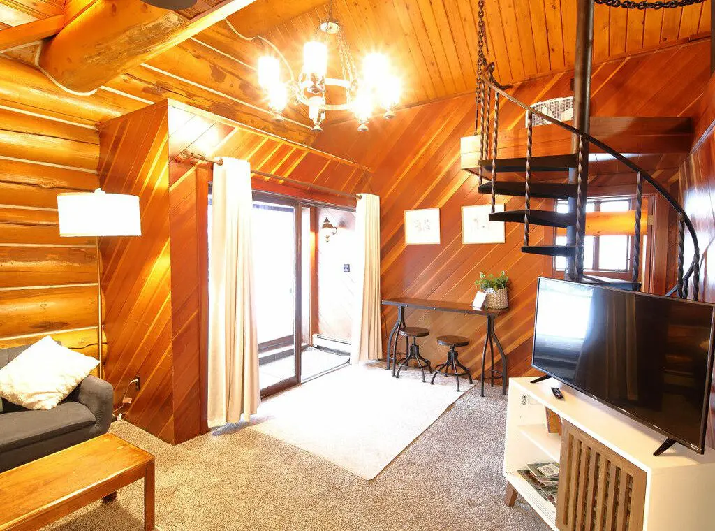 Warm log cabin living room in Fairbanks Alaska with wooden interior, couch, and spiral staircase