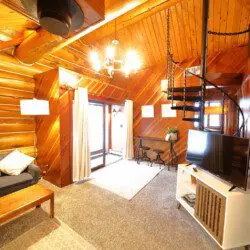 Warm log cabin living room in Fairbanks Alaska with wooden interior, couch, and spiral staircase