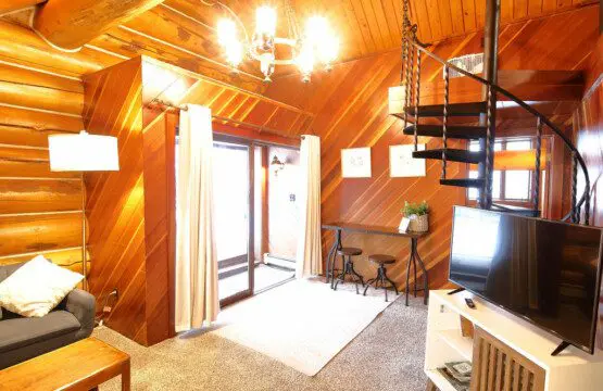 Warm log cabin living room in Fairbanks Alaska with wooden interior, couch, and spiral staircase