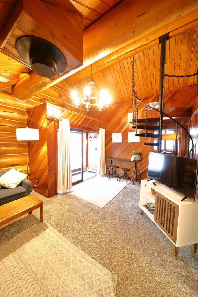 Warm log cabin living room in Fairbanks Alaska with wooden interior, couch, and spiral staircase