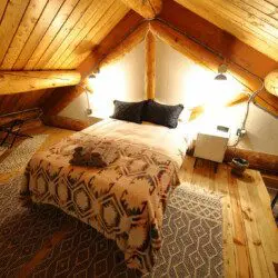 Warmly lit loft bedroom with log beams, patterned bedding, and cozy decor in a Fairbanks Alaska treehouse rental