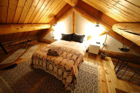 Warmly lit loft bedroom with log beams, patterned bedding, and cozy decor in a Fairbanks Alaska treehouse rental