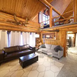 Cozy log cabin living room with stone fireplace, modern sofa, and wood carvings in Fairbanks Alaska