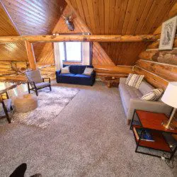 Rustic loft lounge with log walls, cozy seating, and soft carpet in a Fairbanks Alaska treehouse rental