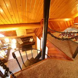 Interior view of a log cabin in Fairbanks with a black spiral staircase, chandelier, TV stand, and rustic wood accents.
