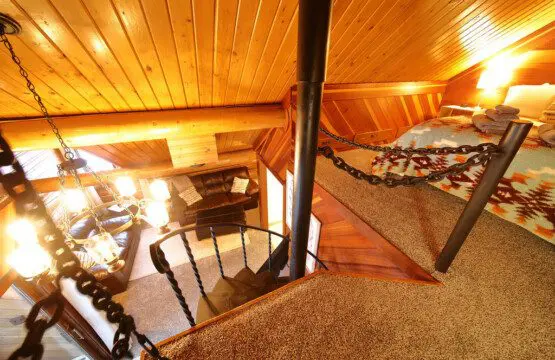 Interior view of a log cabin in Fairbanks with a black spiral staircase, chandelier, TV stand, and rustic wood accents.