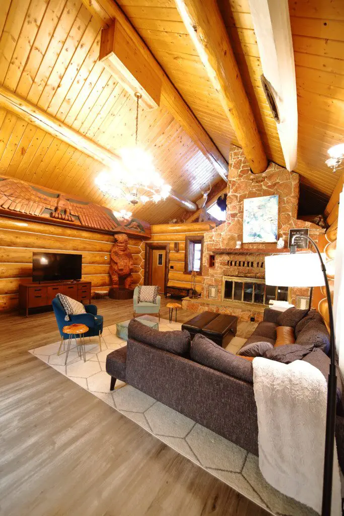 Spacious log cabin living room with wooden beams, cozy seating, and bear carving in Fairbanks, Alaska.