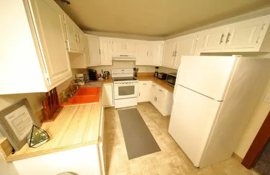 Bright white kitchen with full-size appliances, wooden countertops, and cozy cabin touches at Alaska Adventure Lodge in Fairbanks, Alaska