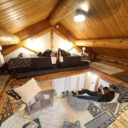 Warmly lit loft bedroom with log beams, patterned bedding, and cozy decor in a Fairbanks Alaska treehouse rental