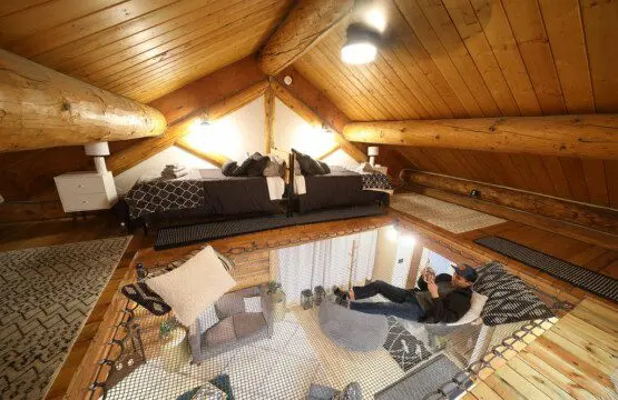 Warmly lit loft bedroom with log beams, patterned bedding, and cozy decor in a Fairbanks Alaska treehouse rental
