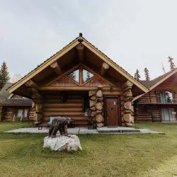 Front view of a log cabin lodge with carved bear sculpture and green lawn at Alaska Adventure Lodge in Fairbanks, Alaska