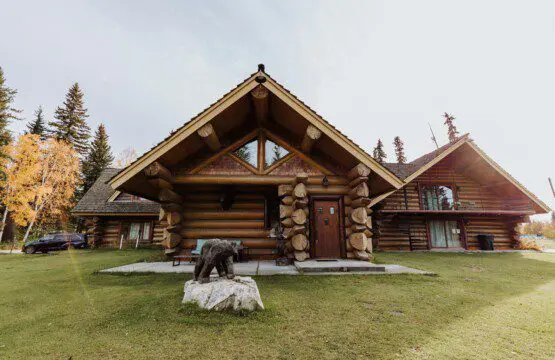 Front view of a log cabin lodge with carved bear sculpture and green lawn at Alaska Adventure Lodge in Fairbanks, Alaska