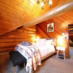 Rustic cabin bedroom with tribal blanket, soft lighting, and wooden walls in a Fairbanks, Alaska treehouse rental.
