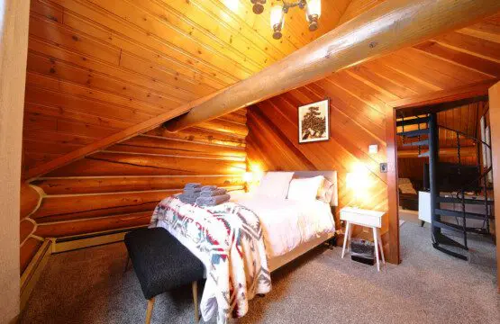 Rustic cabin bedroom with tribal blanket, soft lighting, and wooden walls in a Fairbanks, Alaska treehouse rental.