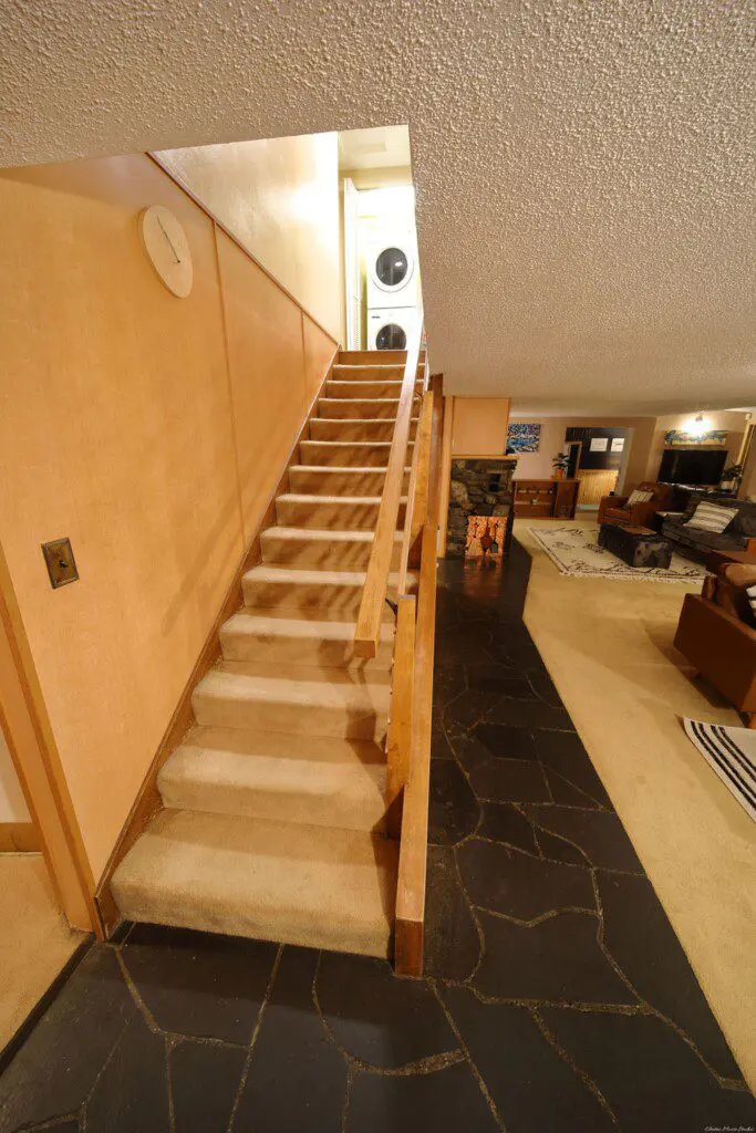 Carpeted staircase leading to upper level with laundry, overlooking cozy living space in Fairbanks Alaska lodge