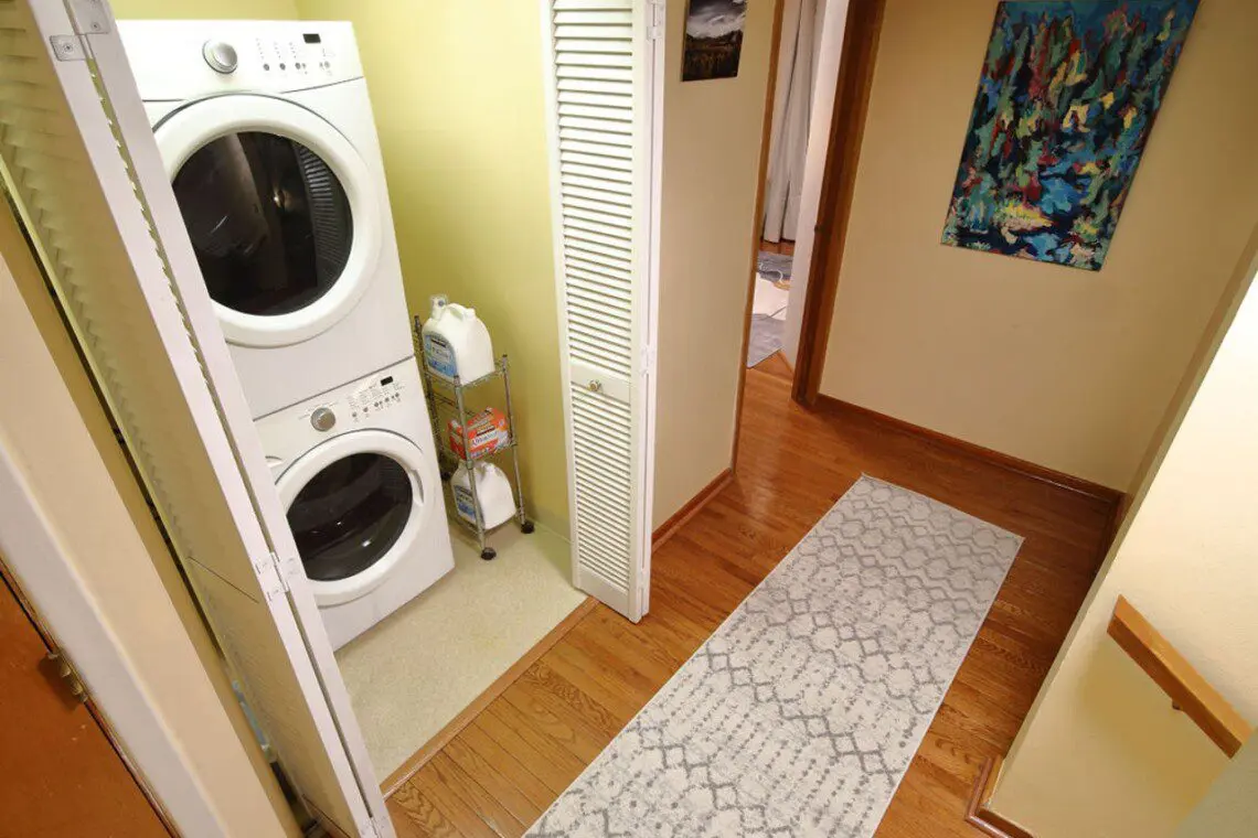 Hallway with stacked washer and dryer unit, rug, and wall art in a Fairbanks Alaska lodge