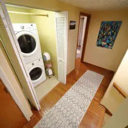 Hallway with stacked washer and dryer unit, rug, and wall art in a Fairbanks Alaska lodge