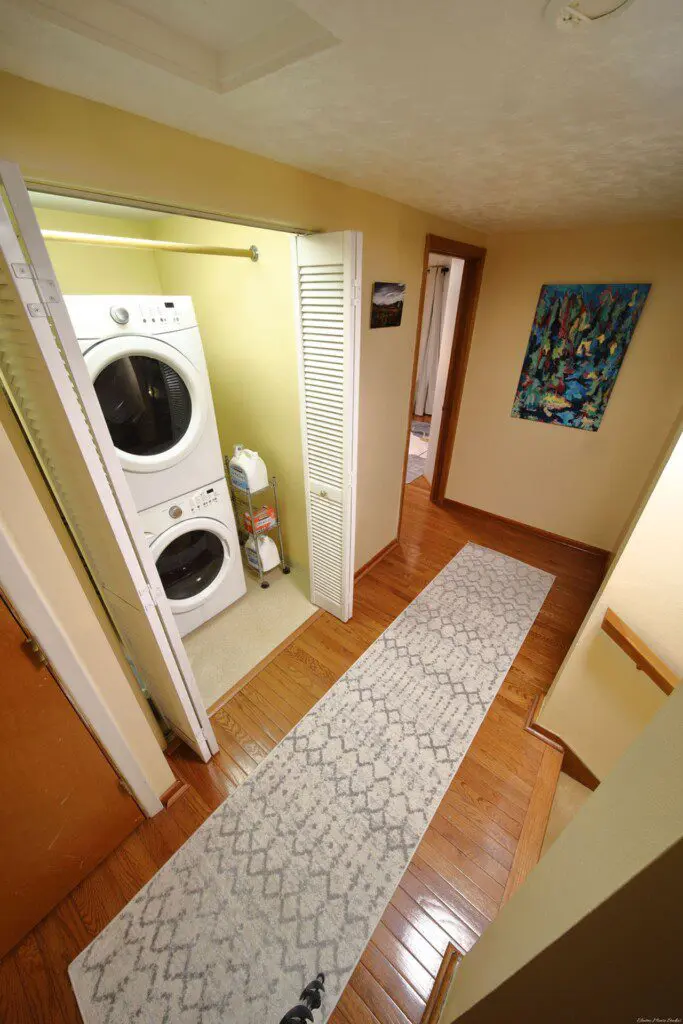 Hallway with stacked washer and dryer unit, rug, and wall art in a Fairbanks Alaska lodge