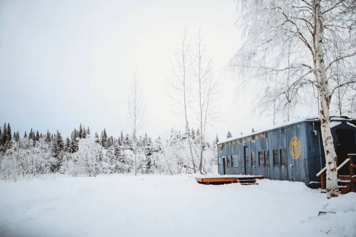 Vintage Alaska Railroad car in snowy Fairbanks forest at unique lodge stay.