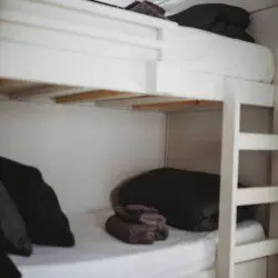 White wooden bunk beds with black pillows and folded towels in a Fairbanks Alaska adventure lodge