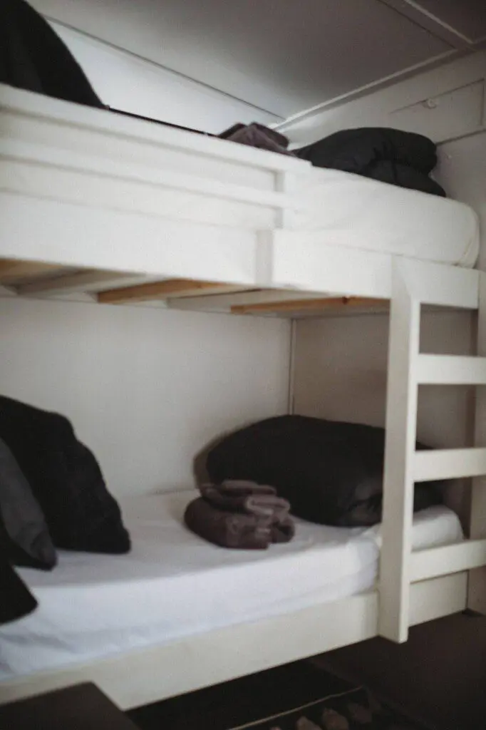 White wooden bunk beds with black pillows and folded towels in a Fairbanks Alaska adventure lodge