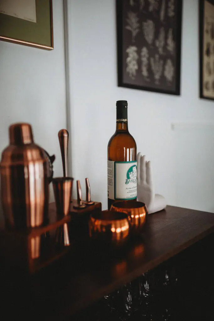 Bottle of alcohol with copper bar tools and mugs on a wooden counter in a Fairbanks Alaska lodge rental