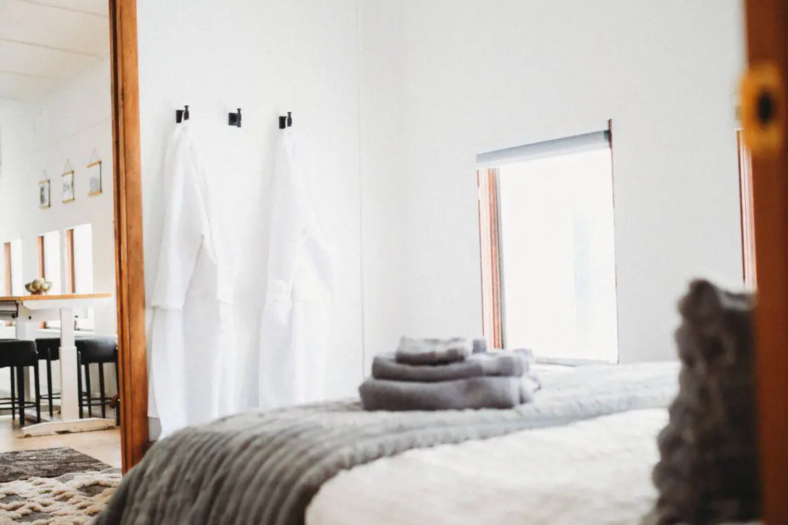Softly lit bedroom with folded towels, white robes, and large windows in a Fairbanks Alaska lodge