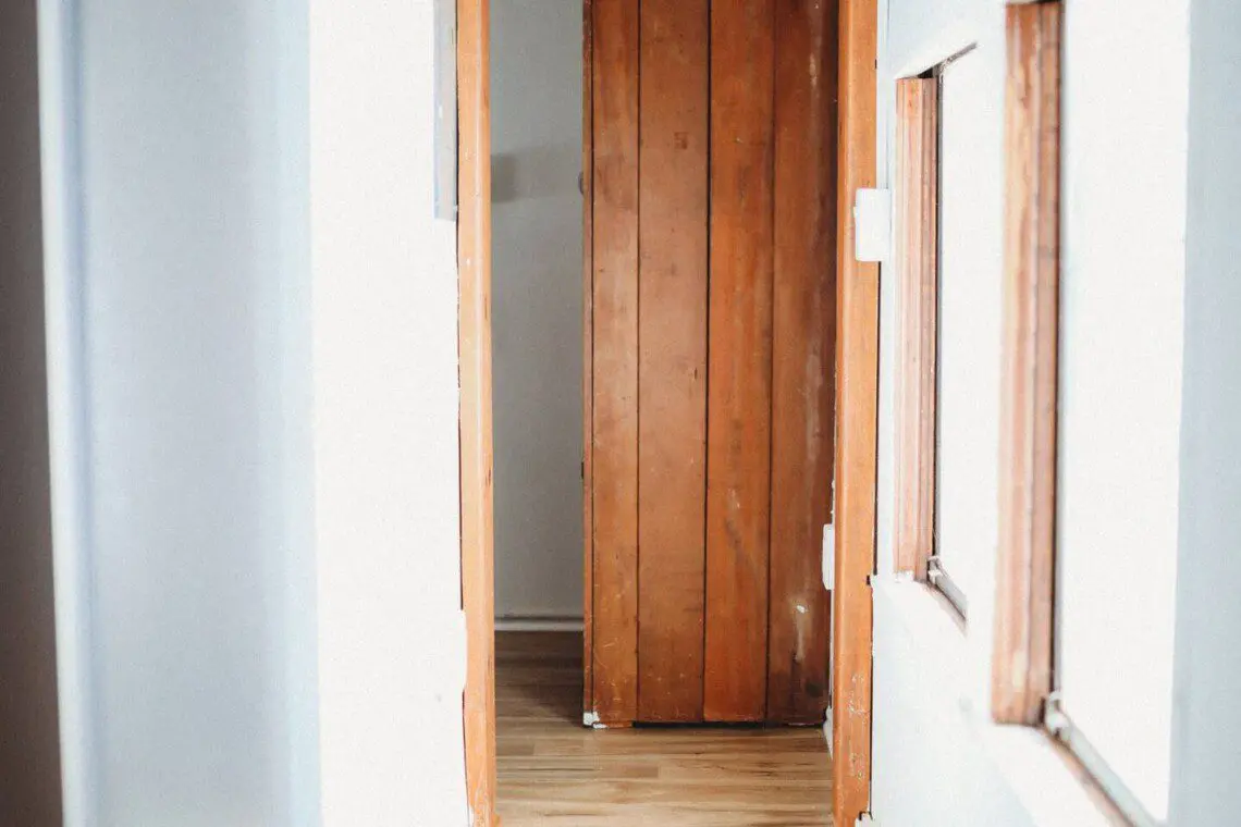 Narrow hallway with wooden door, white walls, and natural light in a Fairbanks Alaska adventure lodge