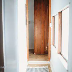 Narrow hallway with wooden door, white walls, and natural light in a Fairbanks Alaska adventure lodge