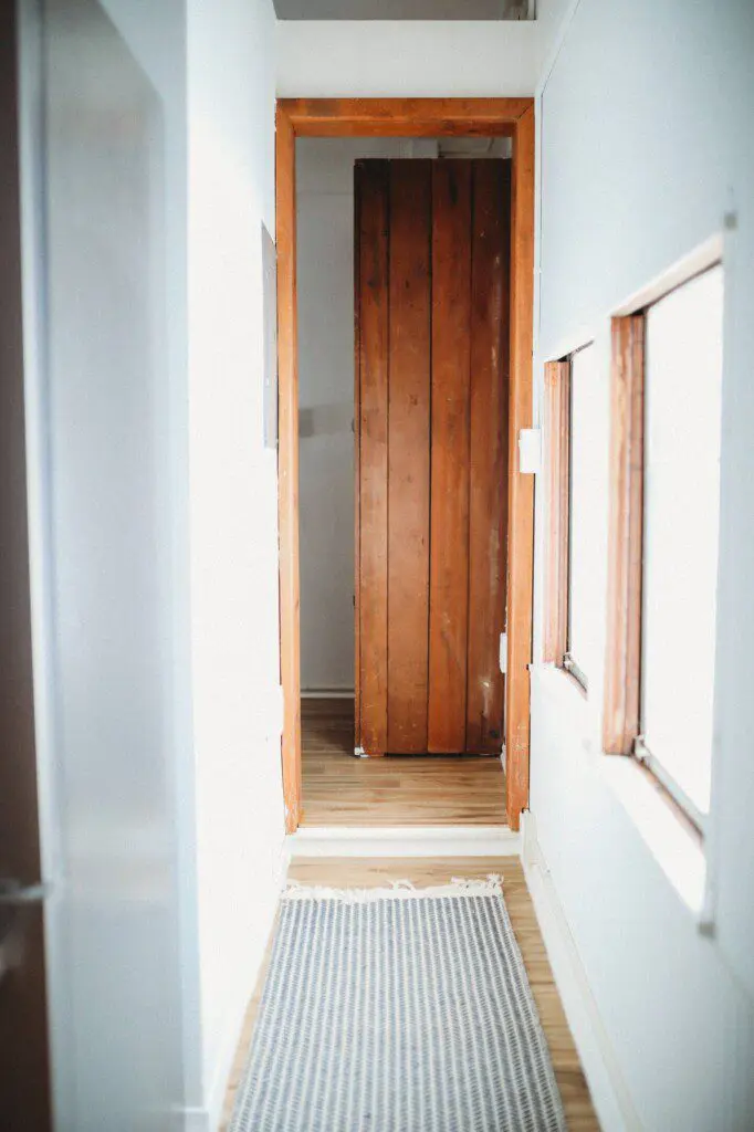 Narrow hallway with wooden door, white walls, and natural light in a Fairbanks Alaska adventure lodge
