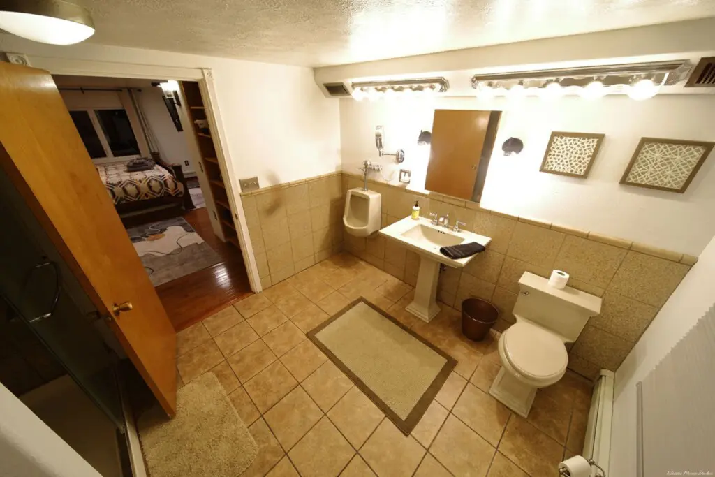Well-lit bathroom with tiled floor, pedestal sink, and view into cozy bedroom in a Fairbanks Alaska lodge