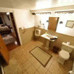 Well-lit bathroom with tiled floor, pedestal sink, and view into cozy bedroom in a Fairbanks Alaska lodge