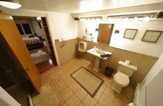 Well-lit bathroom with tiled floor, pedestal sink, and view into cozy bedroom in a Fairbanks Alaska lodge