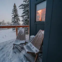 Two wooden chairs on a snow-covered balcony outside a modern treehouse rental in Fairbanks Alaska