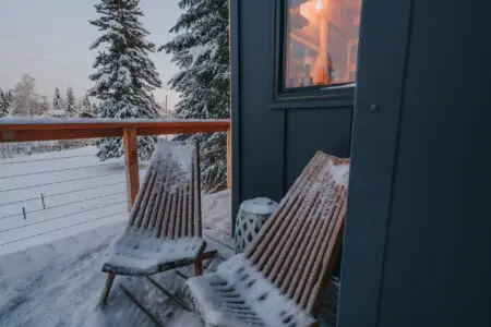 Two wooden chairs on a snow-covered balcony outside a modern treehouse rental in Fairbanks Alaska