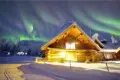 Log cabin in snowy Fairbanks lit under green aurora at an Alaska adventure lodge.