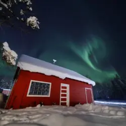 Rustic lodge and red cabin under aurora lights on Chena Pump Road in Fairbanks, Alaska.