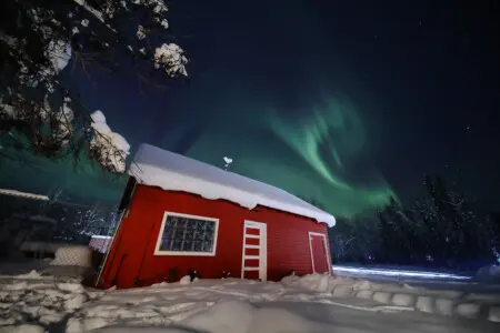 Rustic lodge and red cabin under aurora lights on Chena Pump Road in Fairbanks, Alaska.