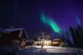 Aurora Borealis glowing above snowy Fairbanks lodge at night, ideal for Alaska adventure and treehouse stays
