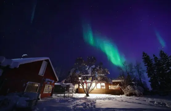 Aurora Borealis glowing above snowy Fairbanks lodge at night, ideal for Alaska adventure and treehouse stays