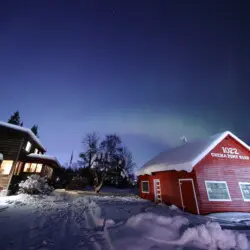 Rustic lodge and red cabin under aurora lights on Chena Pump Road in Fairbanks, Alaska.