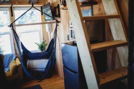 Interior view of a Fairbanks Alaska treehouse with hammock chair, mini fridge, microwave, and wooden loft ladder