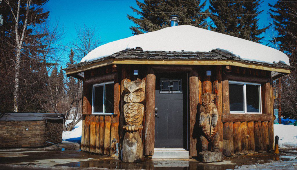 Rustic round wooden cabin with carved totem pillars and snowy roof in Fairbanks Alaska