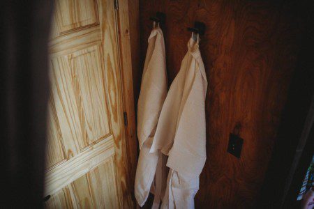 Two soft robes hanging on rustic hooks beside a wooden door in a Fairbanks Alaska treehouse