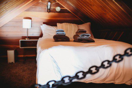 Cozy loft bed with folded towels and wood-paneled walls in Fairbanks Alaska treehouse