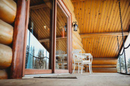 Rustic wood balcony with outdoor seating at a Fairbanks Alaska treehouse overlooking forest