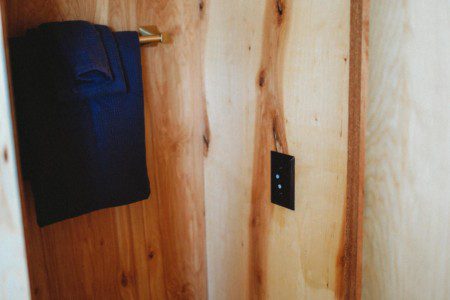 Small wood-paneled closet area with towel hanging on a brass hook in a Fairbanks Alaska treehouse rental  Caption: